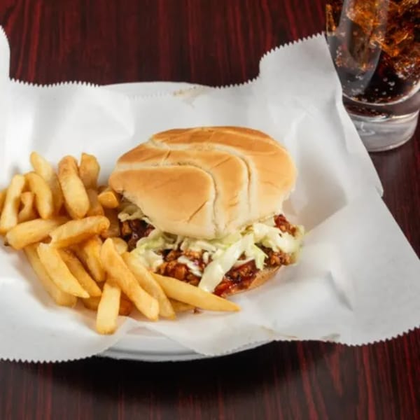 A pulled pork sandwich with coleslaw and fries, served with a soda at GEE STREET KITCHEN.