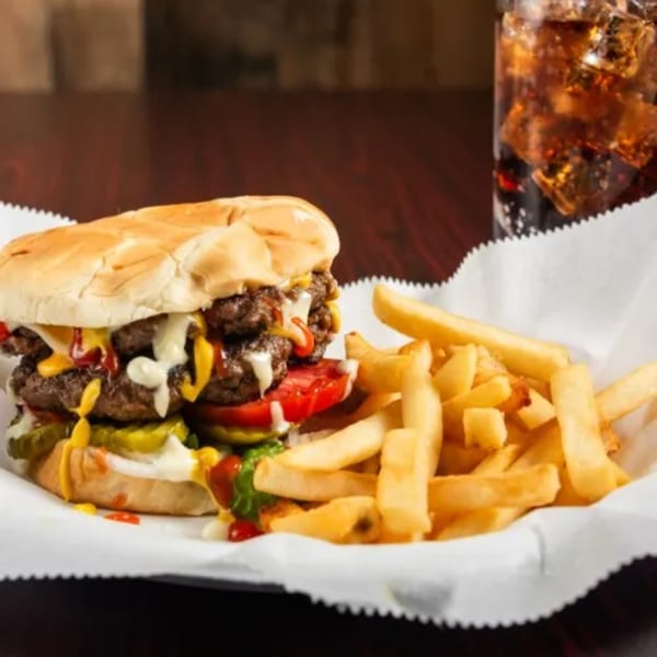 Double cheeseburger with fries and a soda, served in a white paper basket.